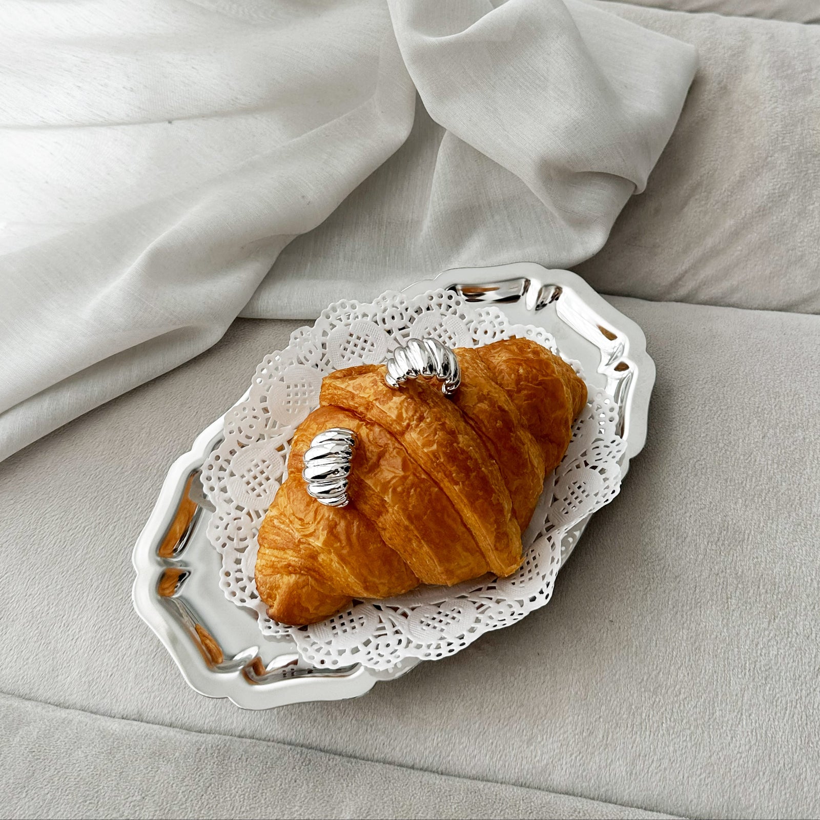 Croissant on a decorative plate with a silver earring on a light gray surface