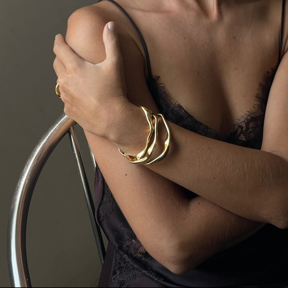 Woman wearing a black lace top with gold jewelry against a neutral background