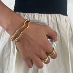 Hand wearing a gold ring and gold bangle bracelet on a white background