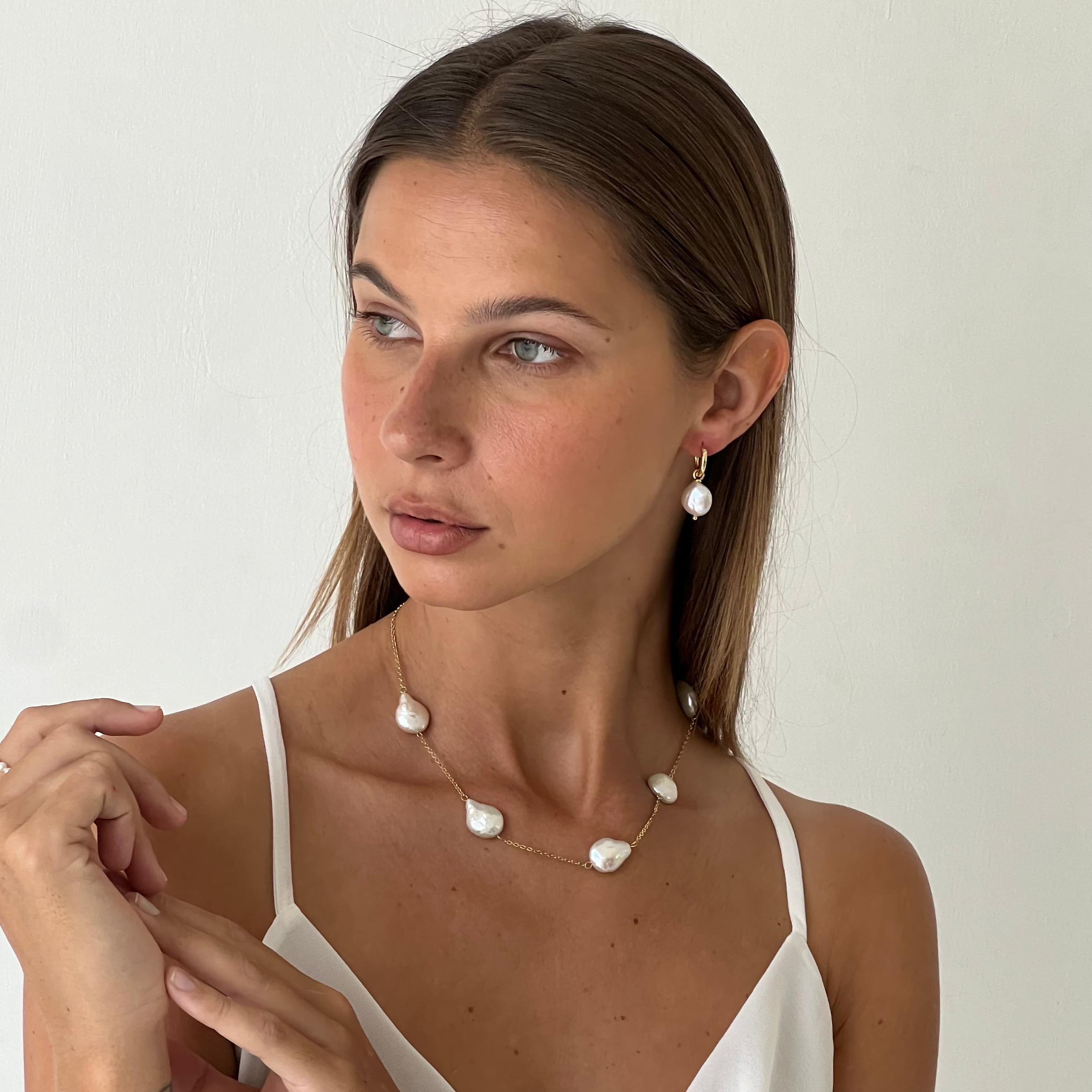 Woman wearing a white dress and pearl necklace jewelry against a plain background