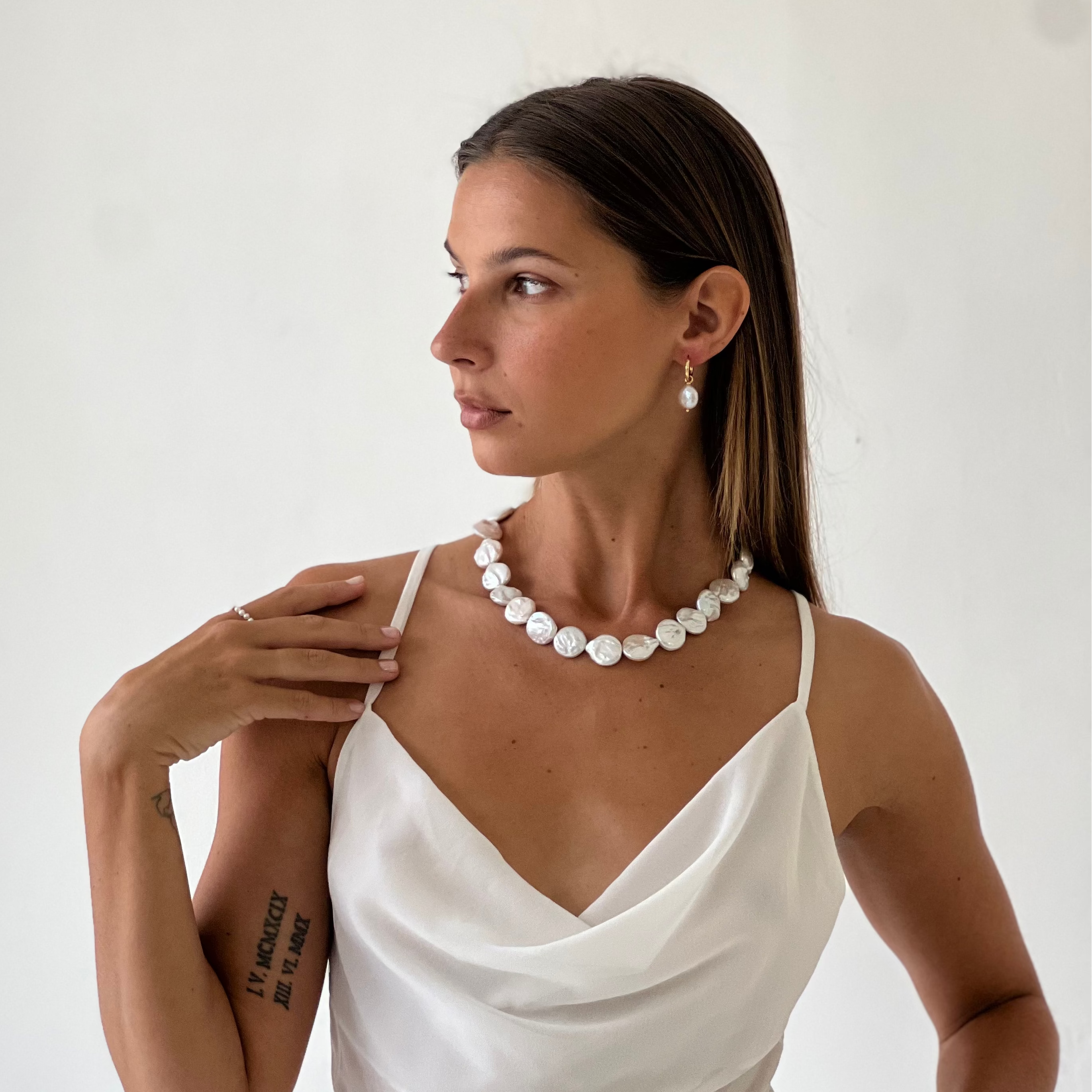 Woman wearing a white dress and pearl necklace against a plain background