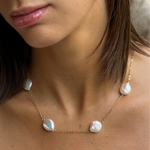 A close-up image of a woman's neck wearing a gold necklace with freshwaterpearls.