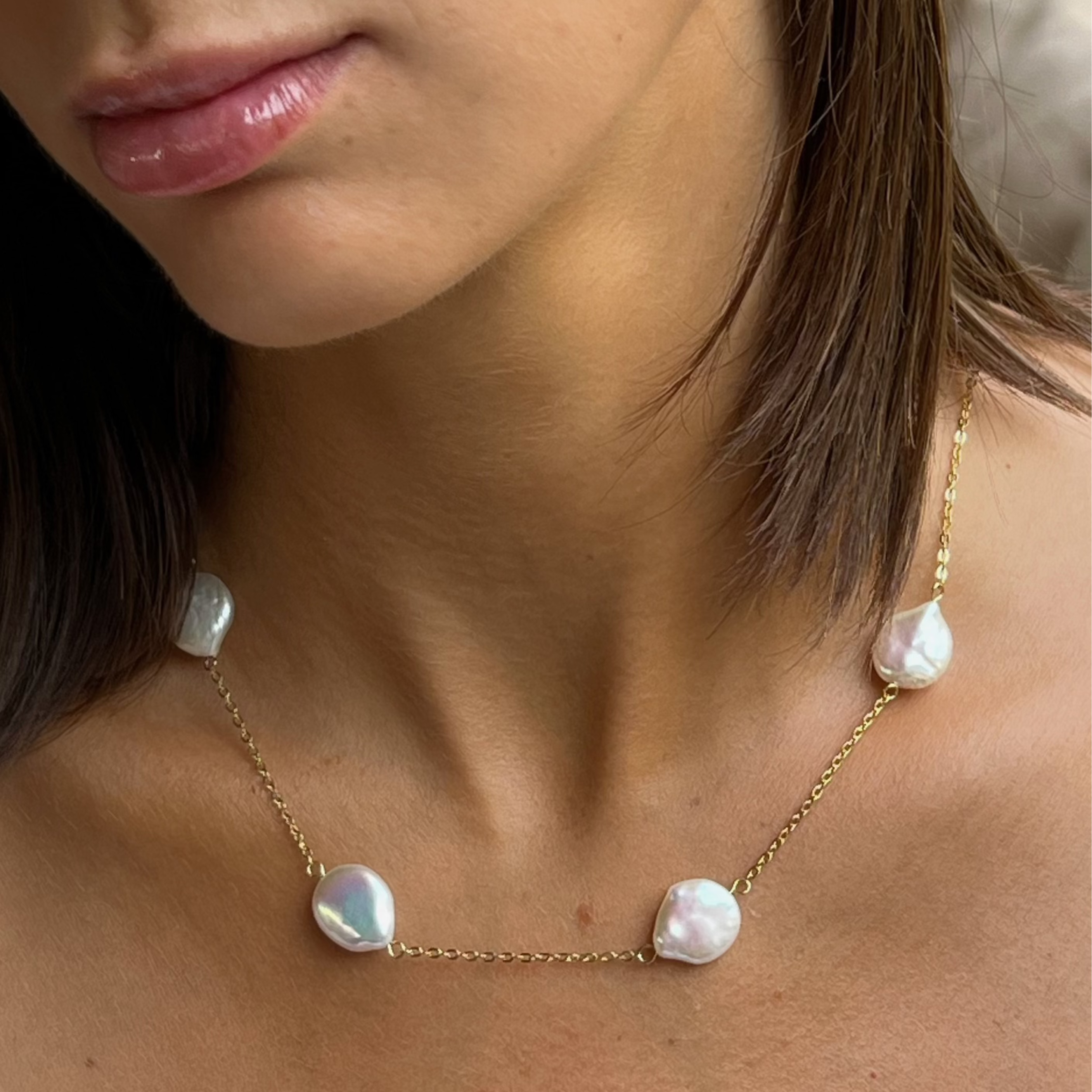 A close-up image of a woman's neck wearing a gold necklace with freshwaterpearls.