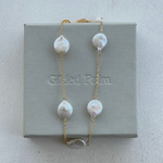 A gold necklace with baroque pearls displayed on a grey box with the brand 'Gifted Palm' inscribed.
