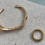 A gold hook bracelet displayed on a textured surface, with a close-up inset showing the bracelet's gold plated and design.