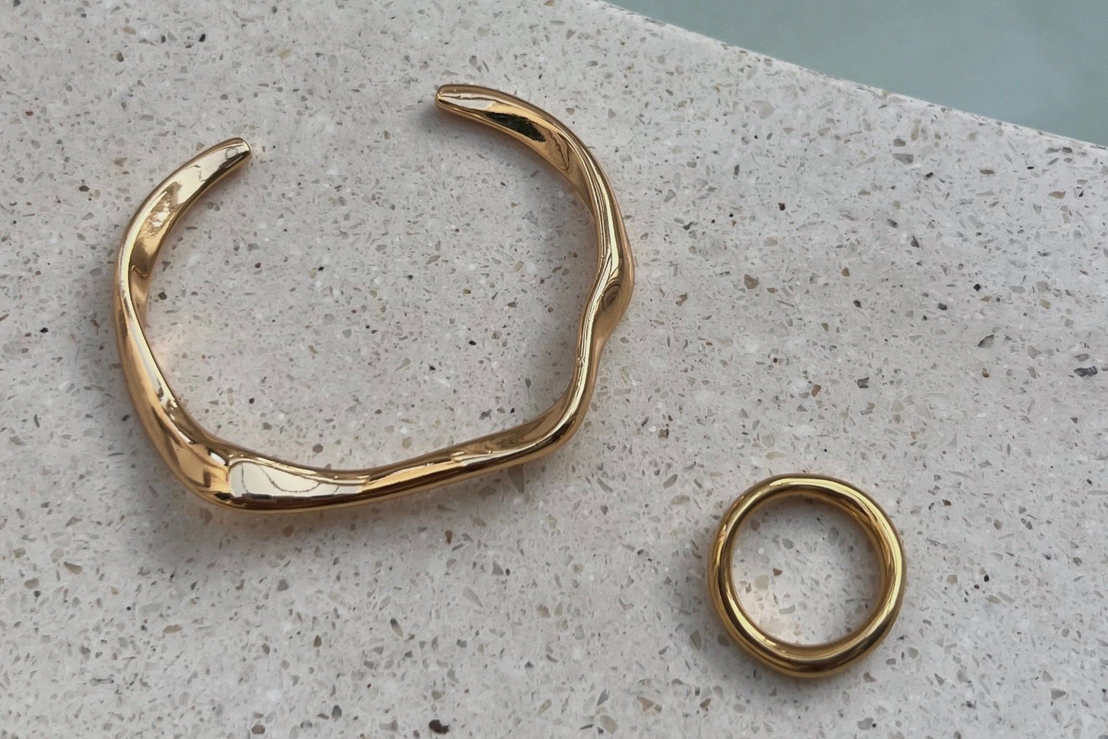 A gold hook bracelet displayed on a textured surface, with a close-up inset showing the bracelet's gold plated and design.